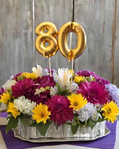 80th Birthday Centerpieces For Tables: Offer A Pop Of Color Colorful floral centerpiece for tables featuring 80th birthday balloon picks.