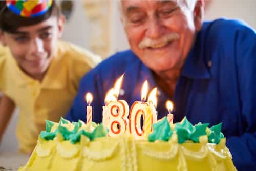 Blow out the candles and make a wish. Man celebrating his 80th Birthday with a decorated cake.
