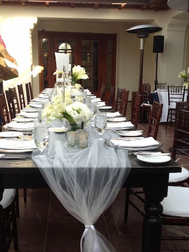 White tulle runner on a rustic wooden table adorned with flowers, candles, and set for an elegant dinner.