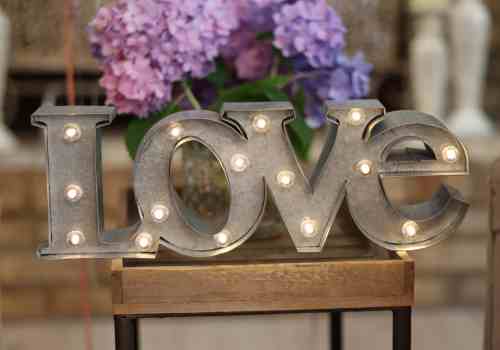 Create a romantic setting with a L-O-V-E sign that glows. Lighted L-O-V-E sign adorned with a vase of fresh flowers.