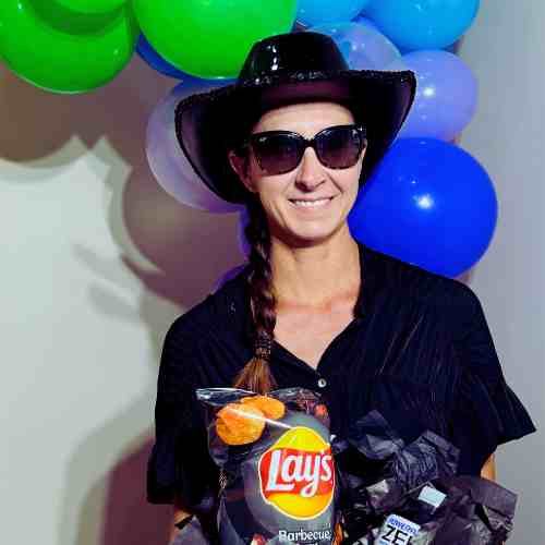 Black Items For Color Party: Think Savory And Sweet Snacks Party guest wearing black sequined hat and dark glasses carrying black items for Color Party.