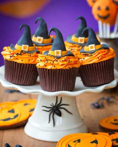 Extend Your Cute Halloween Cupcake Ideas To The Presentation Cute Halloween cupcakes served on a white cake plate with a toy spider crawling up the side.