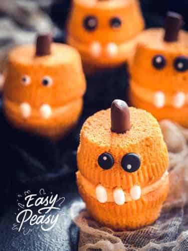 Easy Halloween Cupcake Designs - Quick and Fun Decorating Ideas Two stacked orange cupcakes resembling a pumpkin with a goofy face that is fun and easy to make.