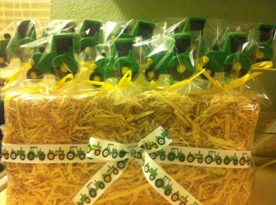 Green tractor lollipops stuck in a hay bale that has been wrapped with tractor ribbon and tied into a bow.