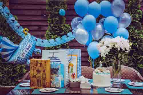 Table decorated for a boy baby shower featuring balloons, banners, and cake in a blue color scheme.