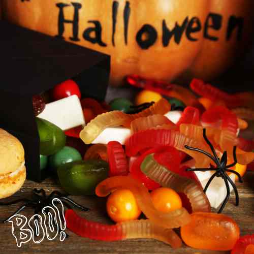 Spooky Haloween Candy, Spiders, And Gummy Worms, Oh My! A Halloween pumpkin surrounded by gummy candy and crawling spiders.